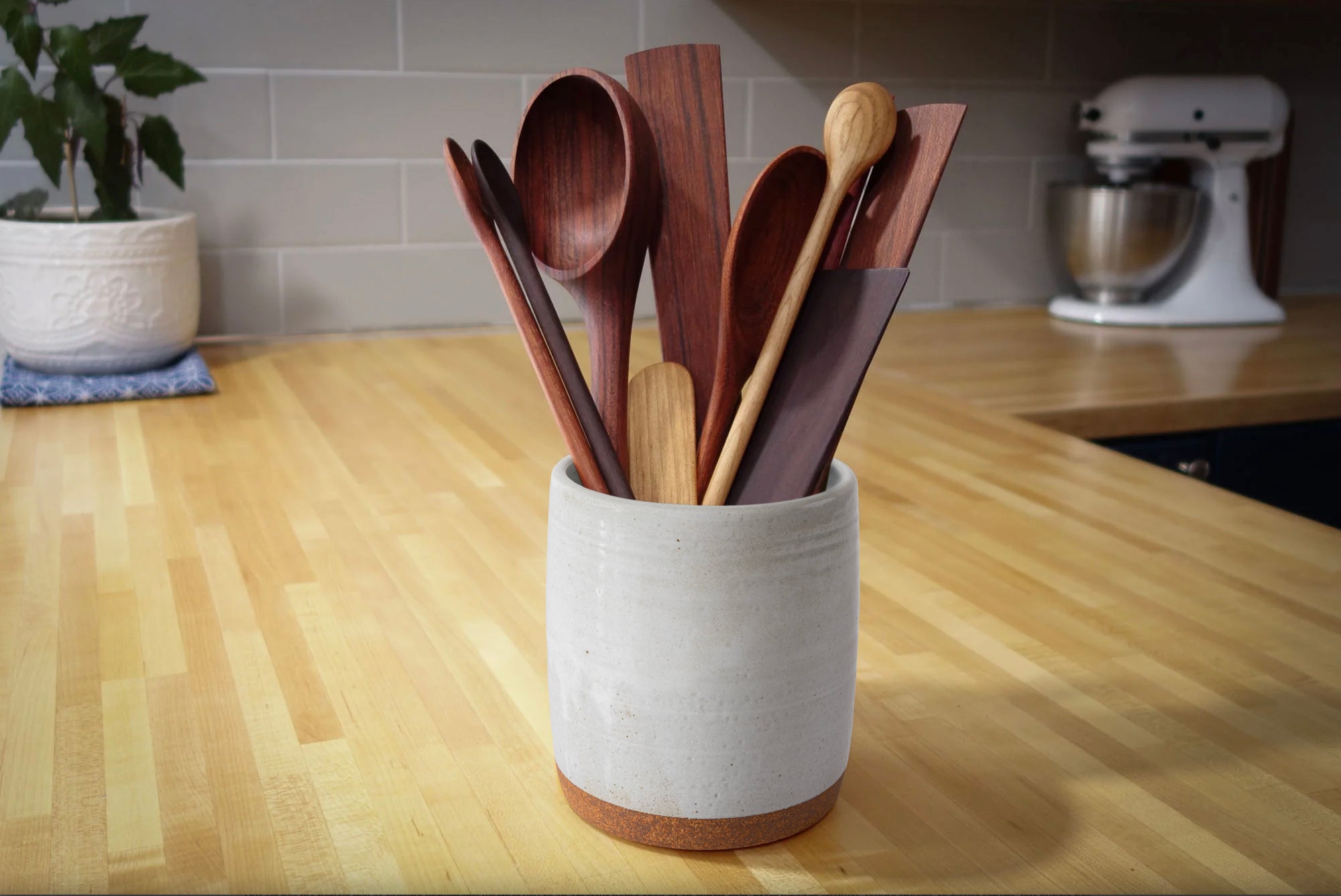 Set of wooden spoons in a white ceramic holder on a kitchen counter.