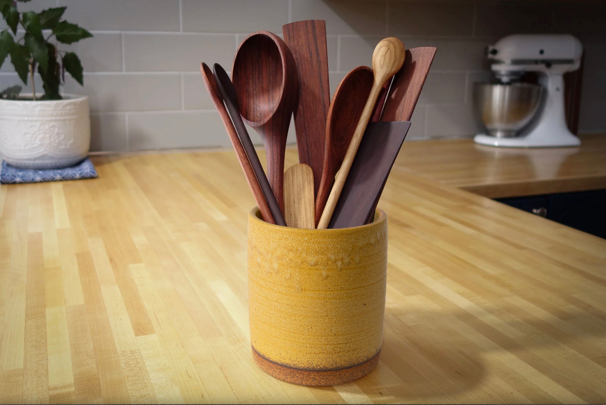 Set of wooden spoons in a yellow container on a kitchen counter.