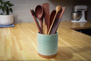 Set of wooden spoons in a green ceramic holder on a kitchen counter.