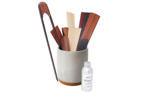 Set of wooden utensils in a container with a bottle labeled 'Wood Care' on a white background