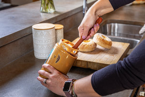 Long wooden spreader digging deep into peanut butter jar