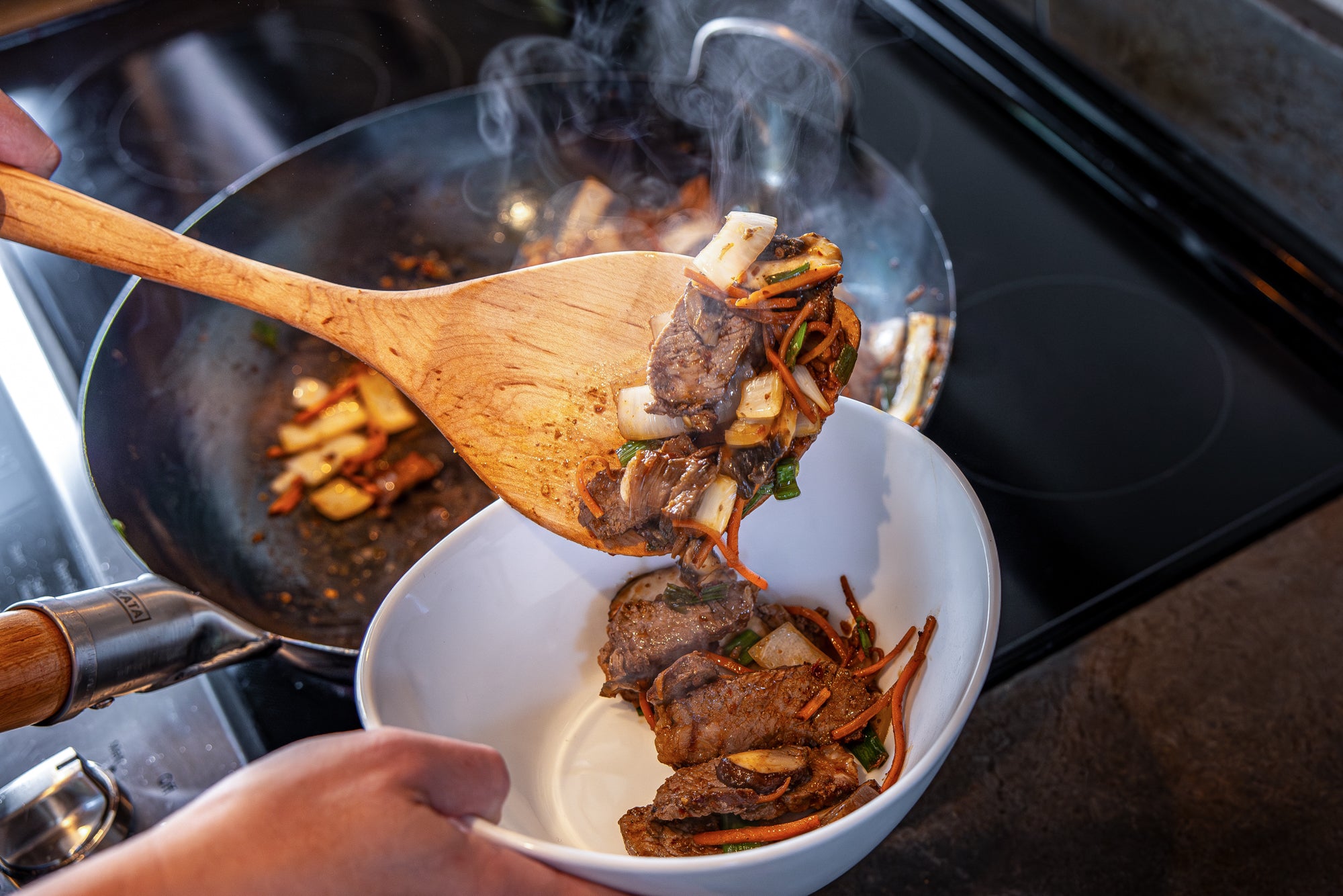 wok spatula serving up steaming stir fry into a bowl from wok