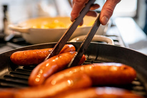 wooden tongs flipping sausages in lodge cast iron pan